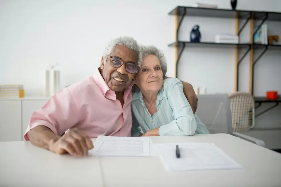 Casal idoso sorridente com papéis e notebook na mesa
