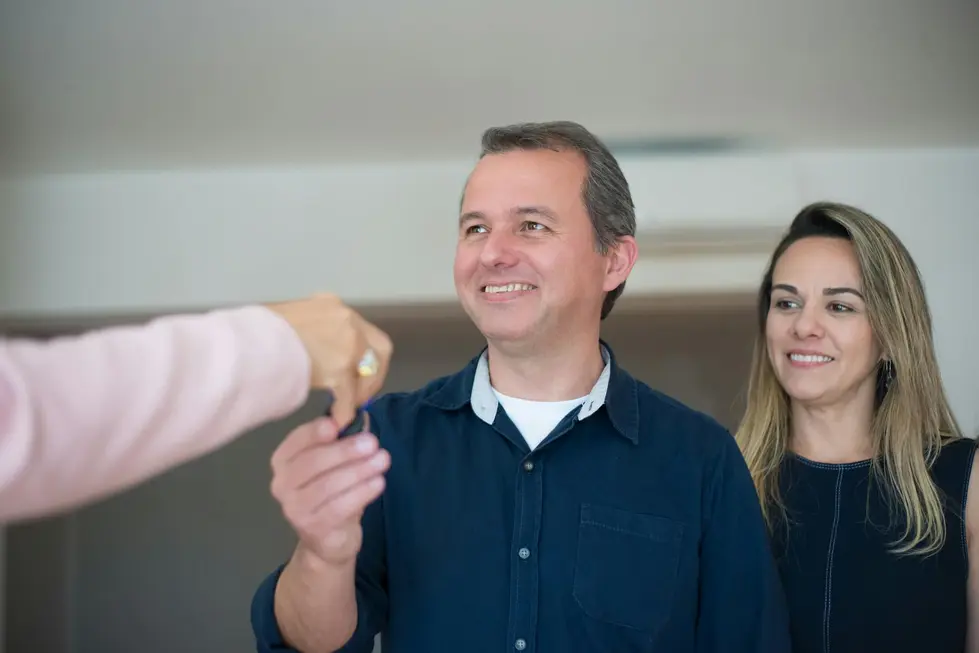 Família sorridente segurando chave em frente a prédio moderno