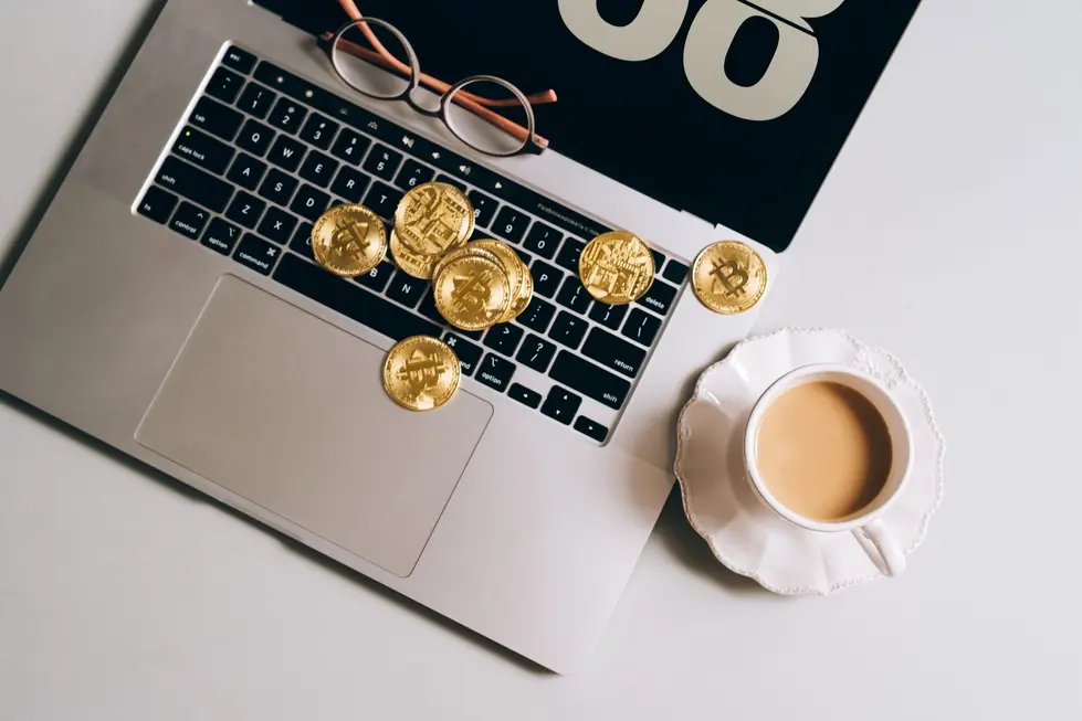 Mesa de café da manhã com laptop mostrando gráficos de Bitcoin e jornal financeiro