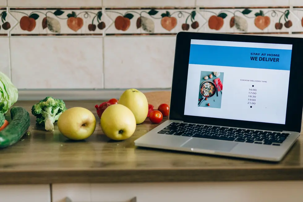 Cozinha iluminada com notebook exibindo app de compras e orçamento